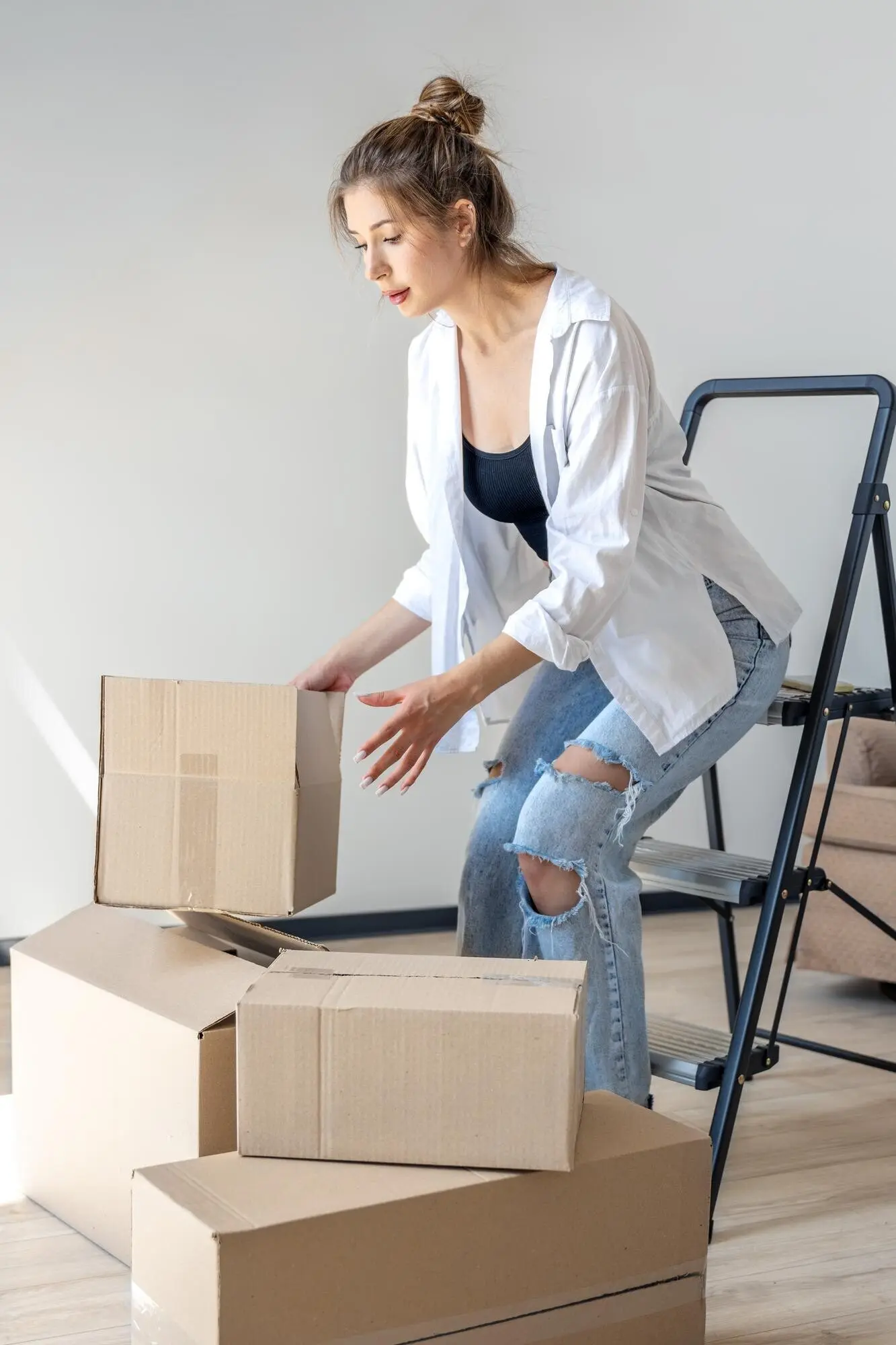 Молодая женщина одна, сосредоточенная и аккуратная, складывает коробки во время переезда.